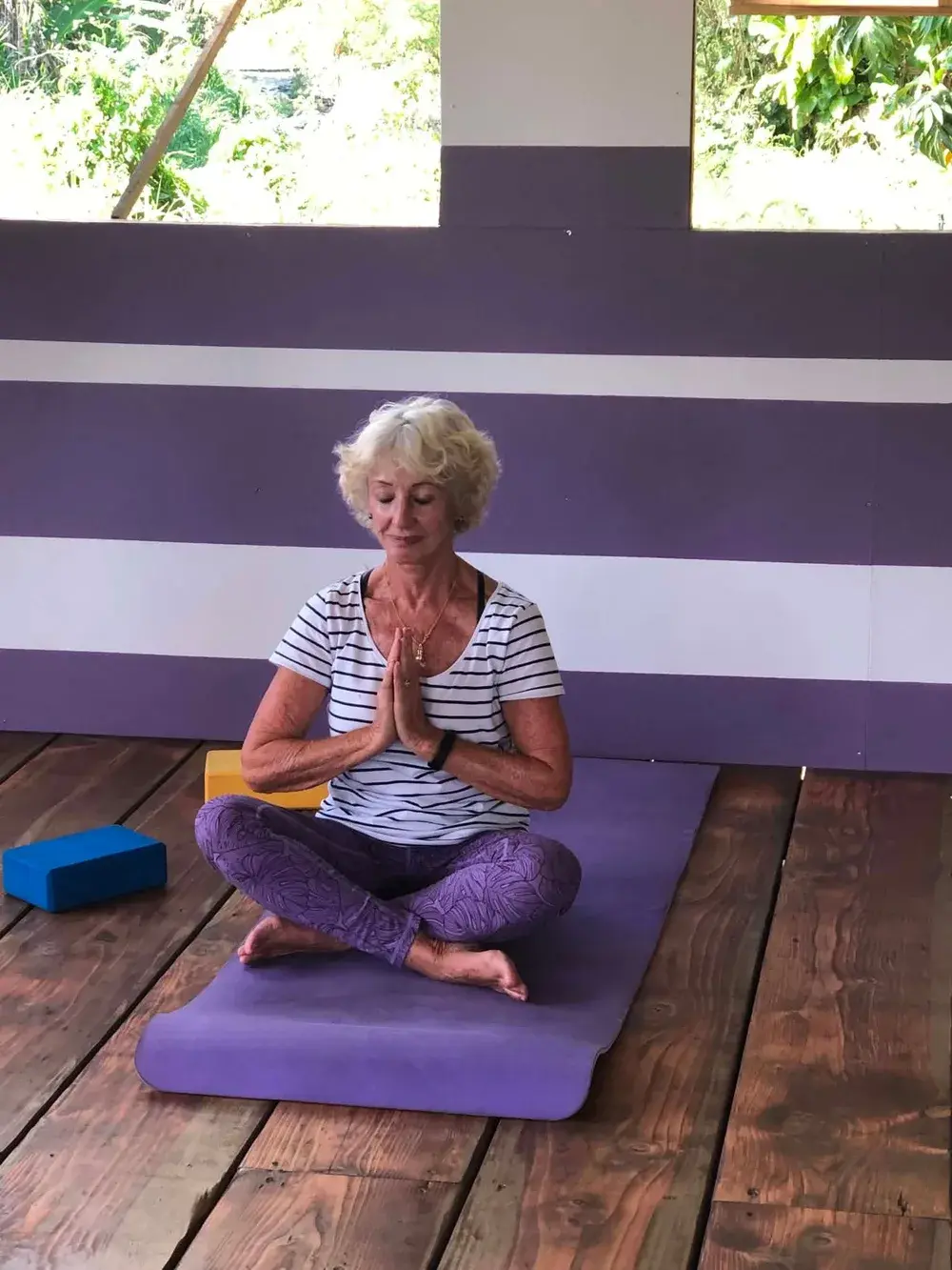 Une élève assise en tailleur sur son tapis, les mains jointes et les yeux fermés.
