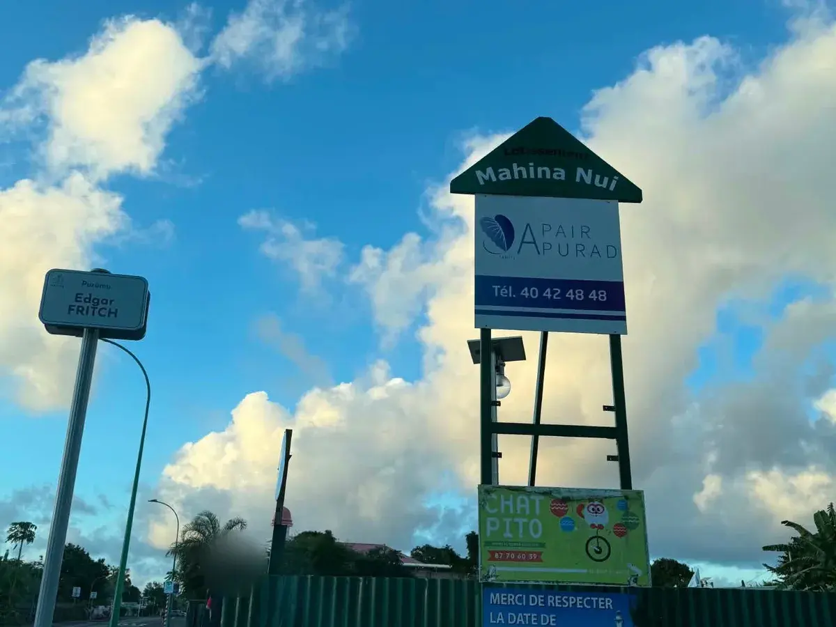 Le panneau « Lotissement Mahina Nui » au bord de la route, sous un ciel de traîne.